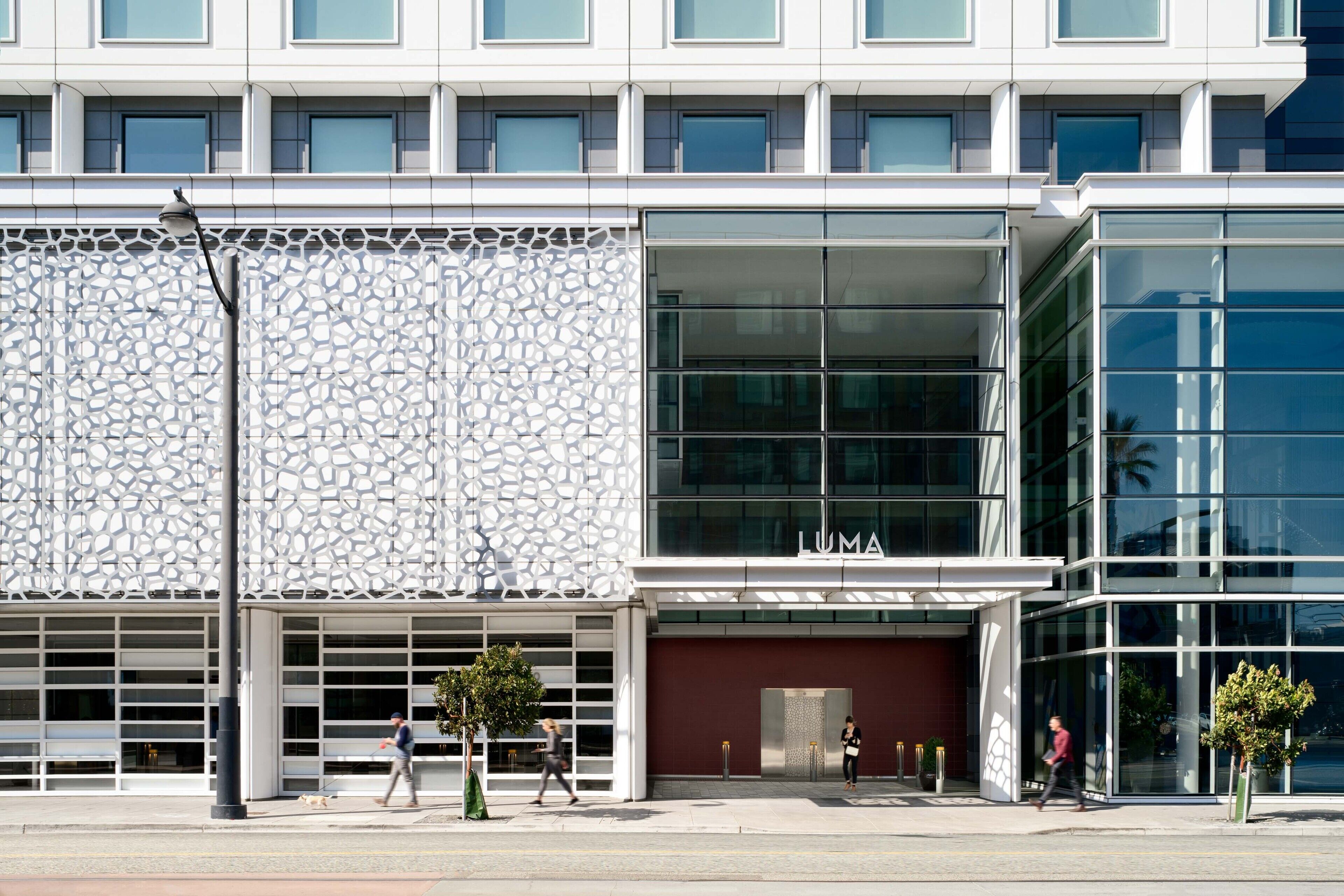 A modern building with a glass facade, a stone-textured wall, and a visible entrance with a red door.