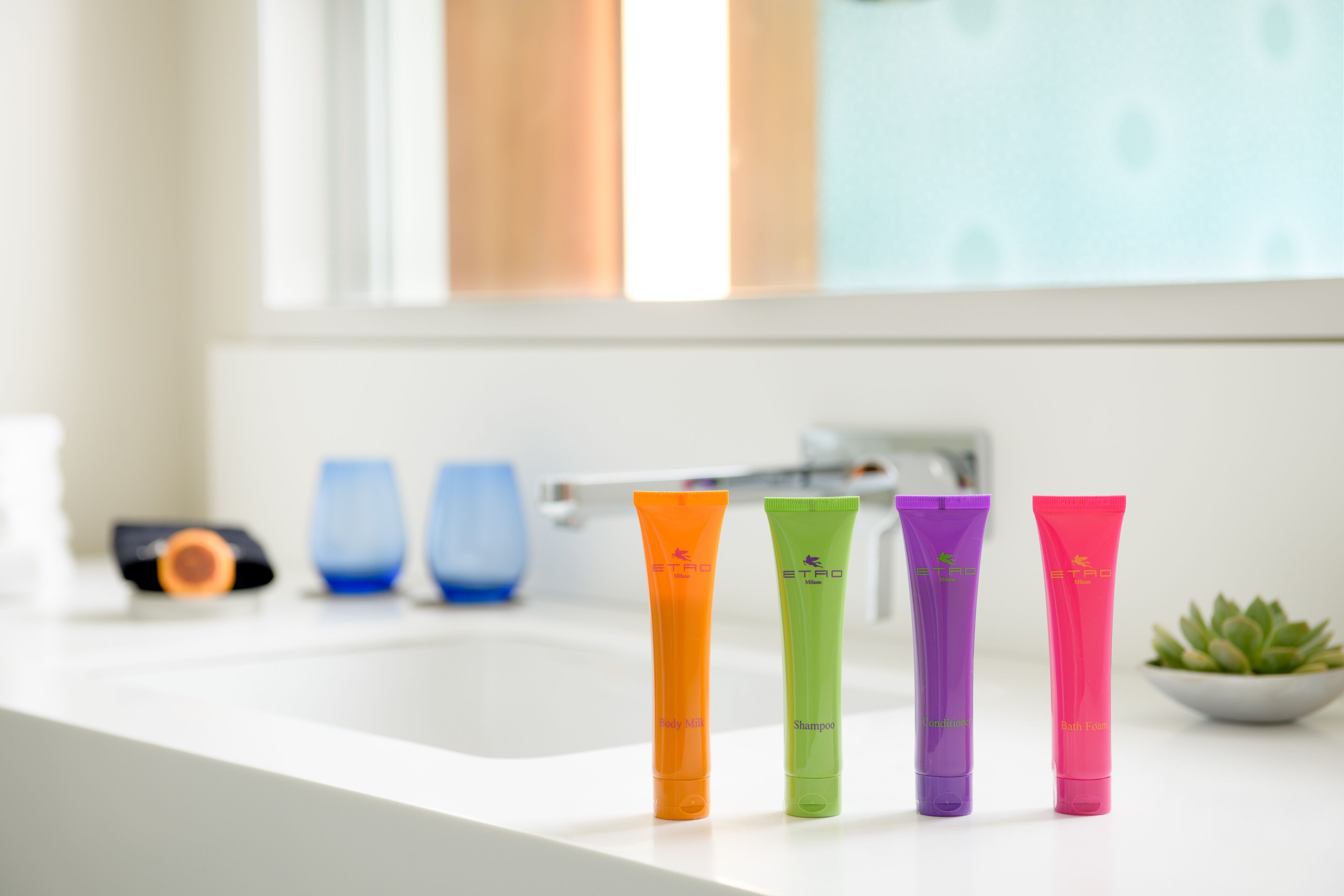 Quatre tubes de shampoing aux couleurs vives sont posés sur le comptoir d’une salle de bain.
