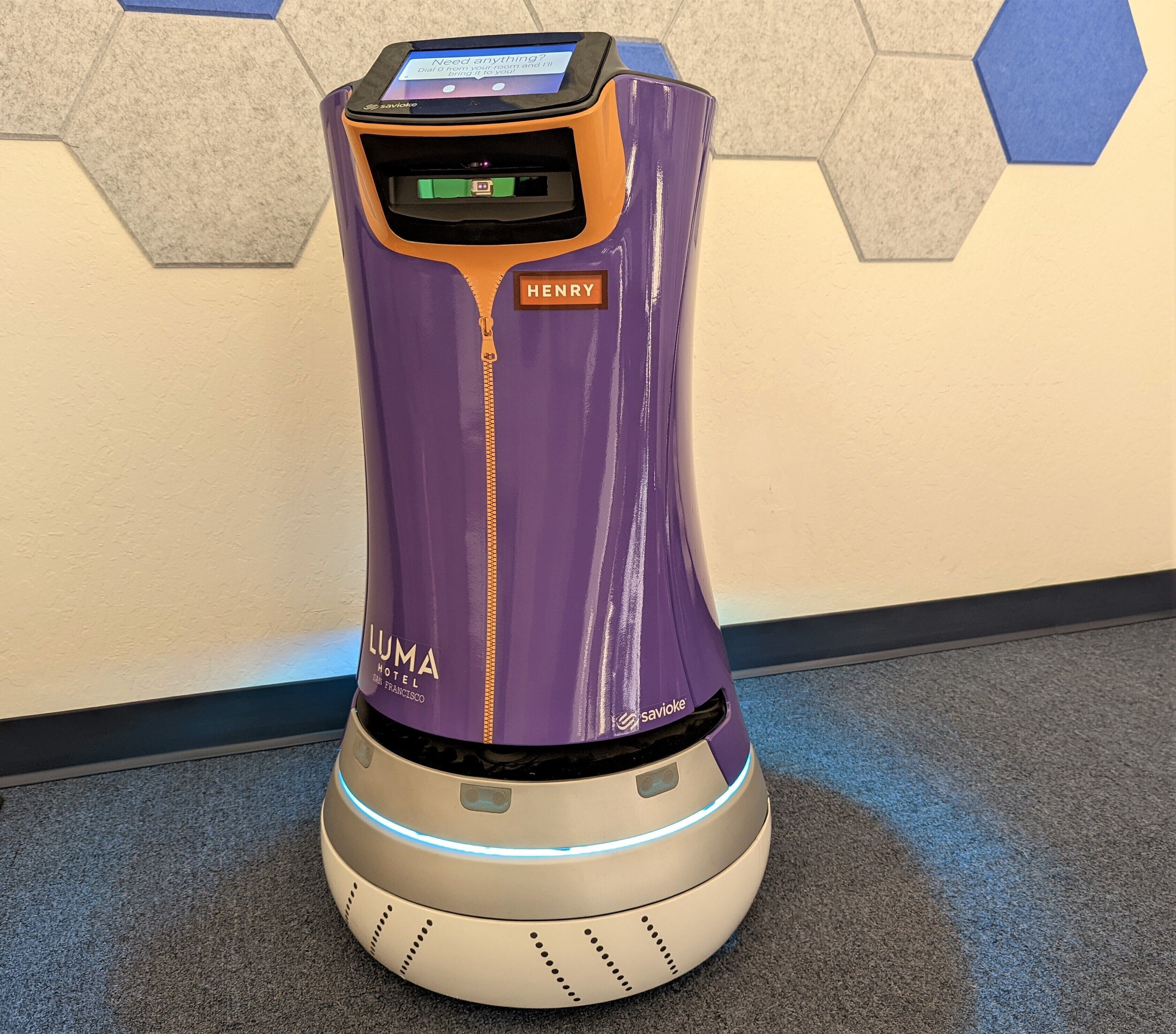 Un robot violet et argenté, doté d’un écran et d’une étiquette où est inscrit le nom « HENRY ».