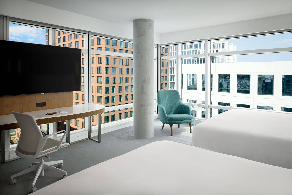 Een moderne hotelkamer met een groot bed, een bureau met stoel, een televisie en een groot raam met uitzicht op de stadszicht.