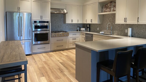 A modern kitchen with stainless steel appliances, wooden flooring, and a central island with bar stools. - Beautiful New Luxury Home - Close to The Village - Amazing Ski In/Out too. (Silver Star Mountain)