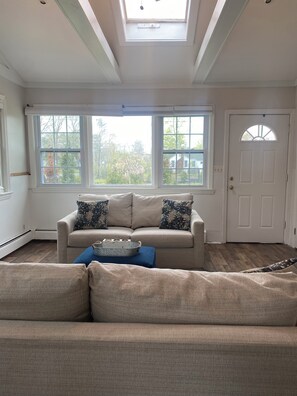 A living room with a beige sofa, a blue ottoman, and a white door.