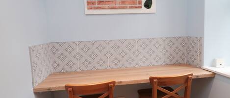 A corner kitchen with a wooden table and two chairs, a backsplash with a geometric pattern, and a wall-mounted art piece of bottles.