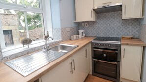 Una cocina con ventana, pileta de acero inoxidable, muebles blancos y horno integrado.