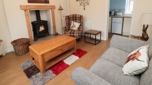 Una sala de estar acogedora con chimenea, un sofá, una mesa de centro de madera y una cocina al fondo.