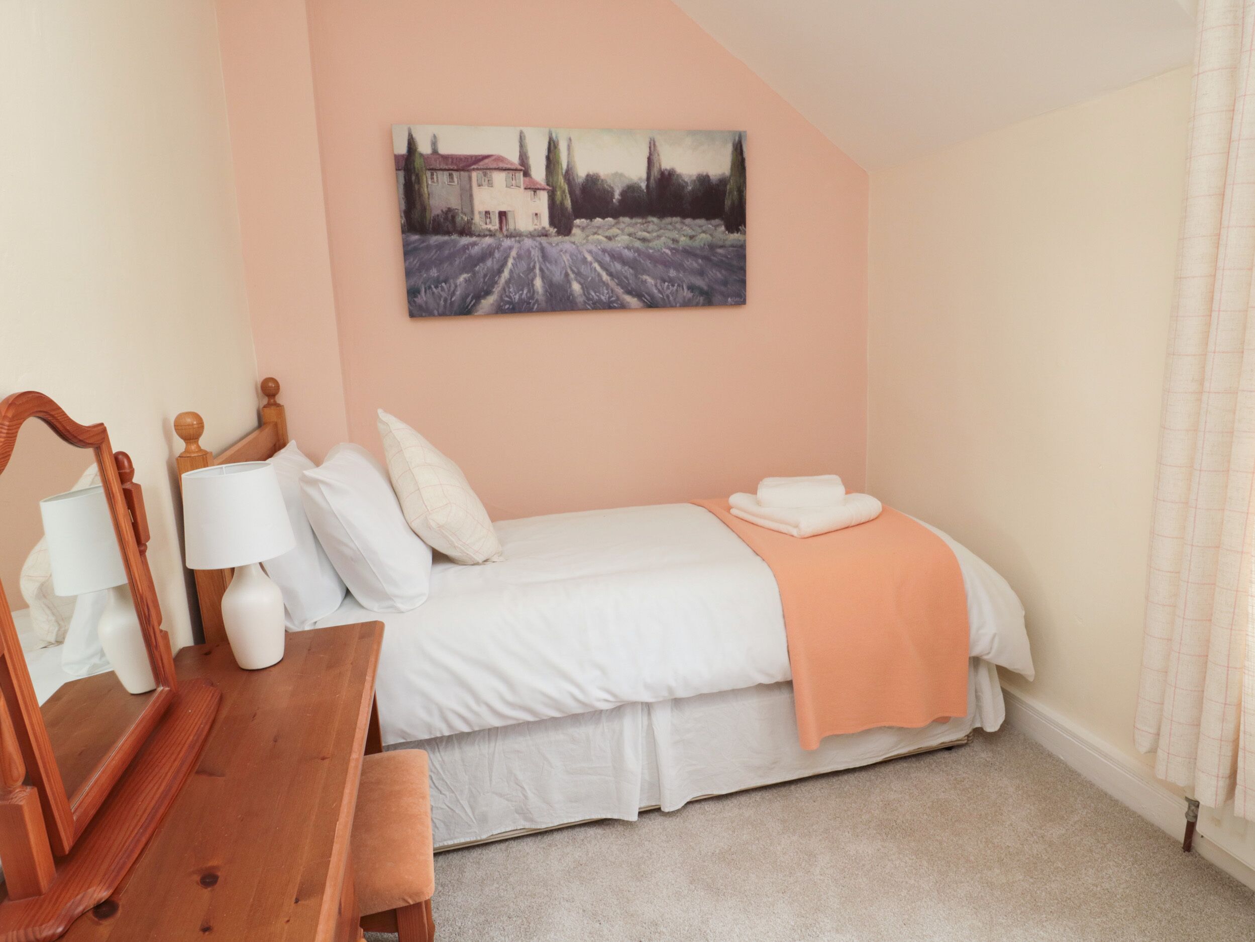 A bedroom with a bed, pillows, a bedside table with lamps, a wooden bench, and a painting on the wall.