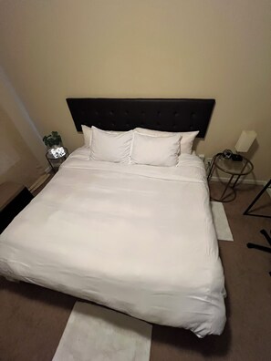 Un letto rifatto con lenzuola bianche, una testata scura e un comodino con una lampada e una piccola pianta.