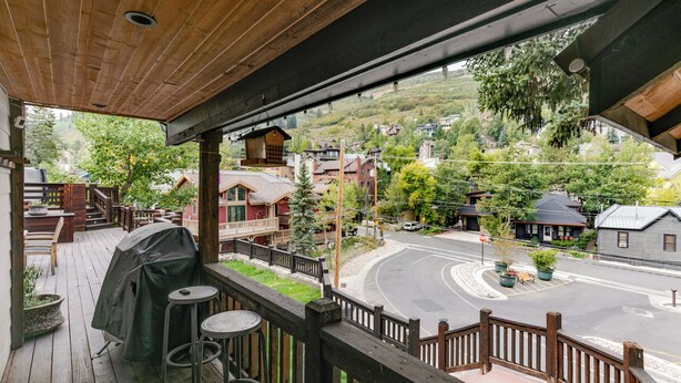 Eine Holzterrasse mit Grillplatz, Gartenmöbeln und Blick auf eine Straße mit Häusern und Grünflächen.