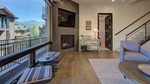 Een moderne woonkamer met een open haard, een balkon met buitenmeubels, en uitzicht op de bergen.
