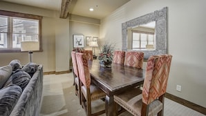 Un comedor con una mesa de madera, sillas estampadas, un sofá y un espejo grande en la pared.