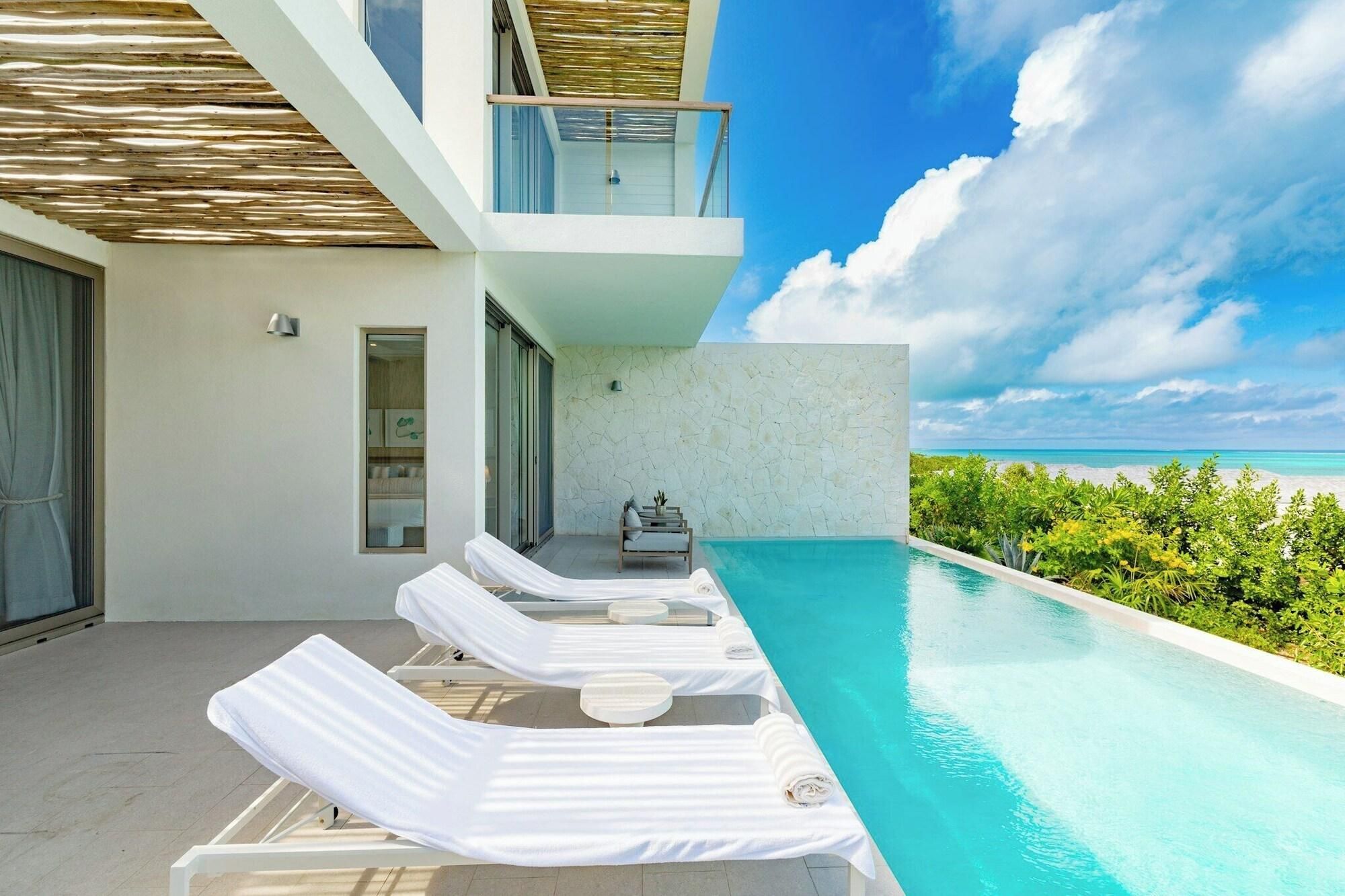 A modern poolside area with lounge chairs, a small seating area, and a view of the ocean.