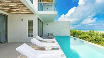 A modern poolside area with lounge chairs, a small seating area, and a view of the ocean.