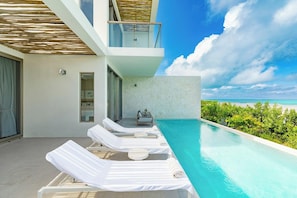 A modern poolside area with lounge chairs, a small seating area, and a view of the ocean.