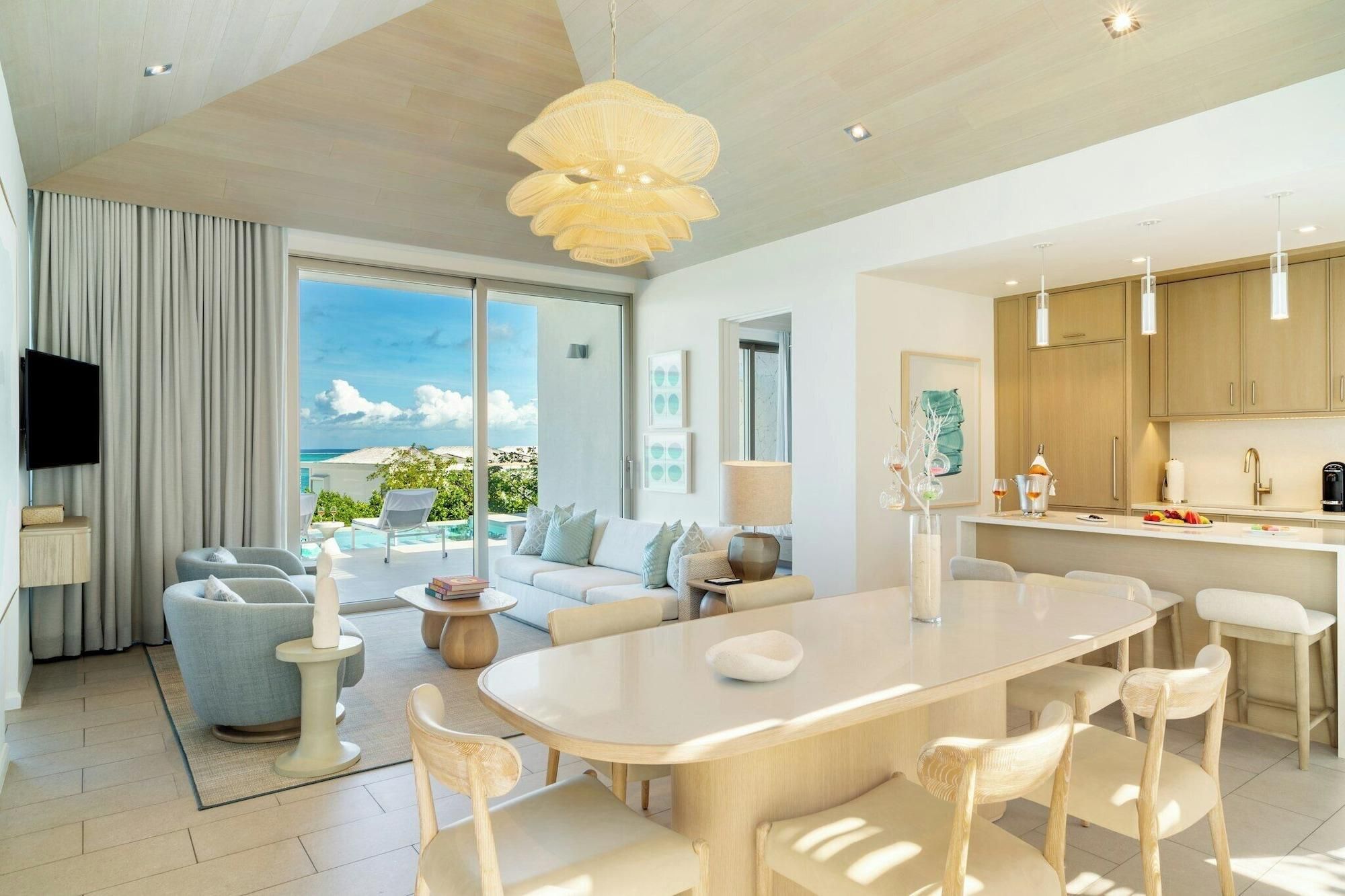 A modern living room with a large window, a dining area, and a kitchen.