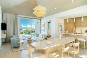 A modern living room with a large window, a dining area, and a kitchen. - Rock House (Providenciales)