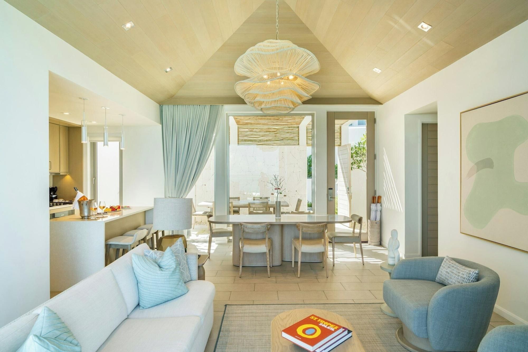 A modern living room with a sofa, armchair, dining area, and a large chandelier.