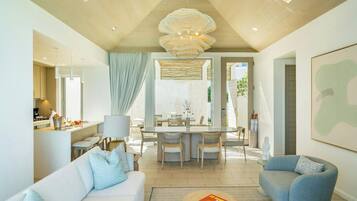 A modern living room with a sofa, armchair, dining area, and a large chandelier.