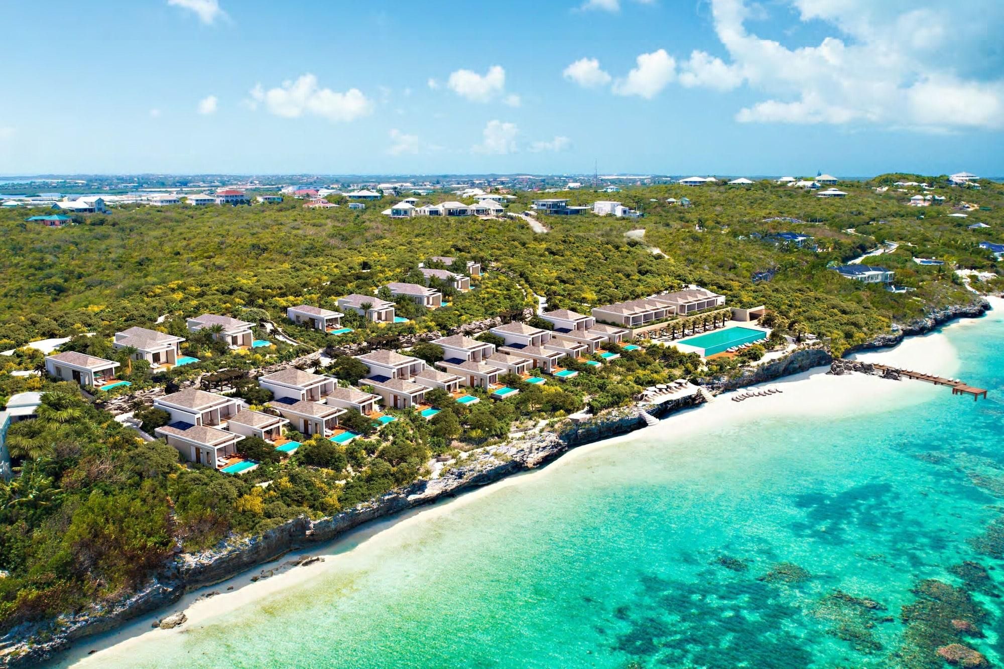 An aerial view of a resort with multiple buildings, a beach, and clear turquoise waters.