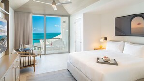 Habitación de hotel con cama, escritorio con silla, balcón y vista al océano, además de ventilador de techo.