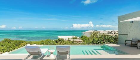 A pool area with lounge chairs and a view of the ocean.