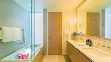 Un baño moderno con ducha de vidrio, bañera con pétalos de rosa, espejo grande y tocador con artículos de aseo.