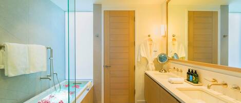 Een moderne badkamer met een douchecabine van glas, een badkuip met rozenblaadjes, een grote spiegel en een wastafel met toiletartikelen.