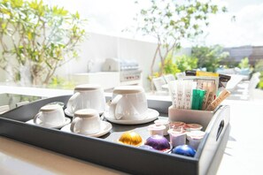 A tray with white cups and saucers, a coffee machine, and a container with coffee pods and a book.