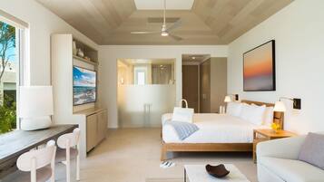 A modern hotel room with a bed, desk, chairs, a TV, and a painting.