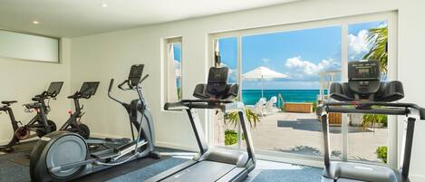 A gym with treadmills, stationary bikes, and a view of the ocean.
