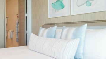 A neatly made bed with white and light blue pillows, a striped towel on a rack, and two abstract art pieces on the wall.