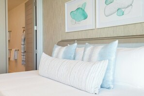 A neatly made bed with white and light blue pillows, a striped towel on a rack, and two abstract art pieces on the wall. - Rock House (Providenciales)