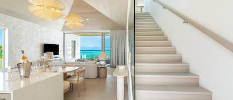 A modern interior with a kitchen, dining area, and a staircase leading to a balcony with a view of the ocean.