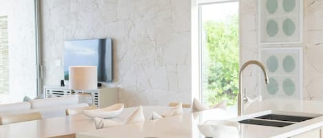 A modern kitchen with a large island, a built-in TV, and a view of greenery outside.