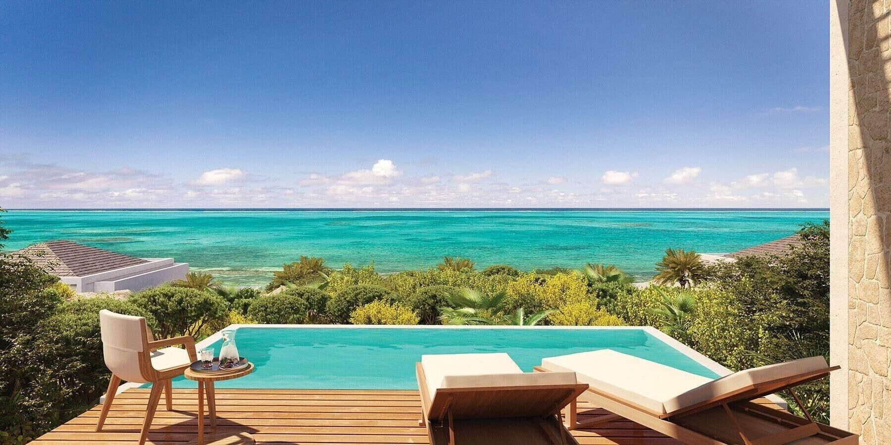 Piscina con vista al océano, terraza de madera y sillas de descanso.