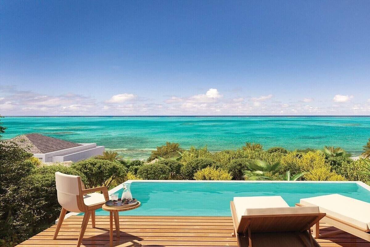 A pool with a view of the ocean, wooden deck, and lounge chairs.