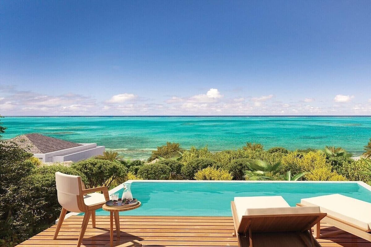 Piscina con vista al océano, terraza de madera y sillas de descanso.