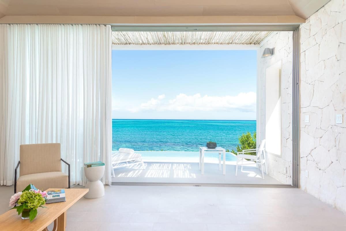 Una habitación con vista al océano, una silla, una mesita con un florero y una silla blanca en el exterior.