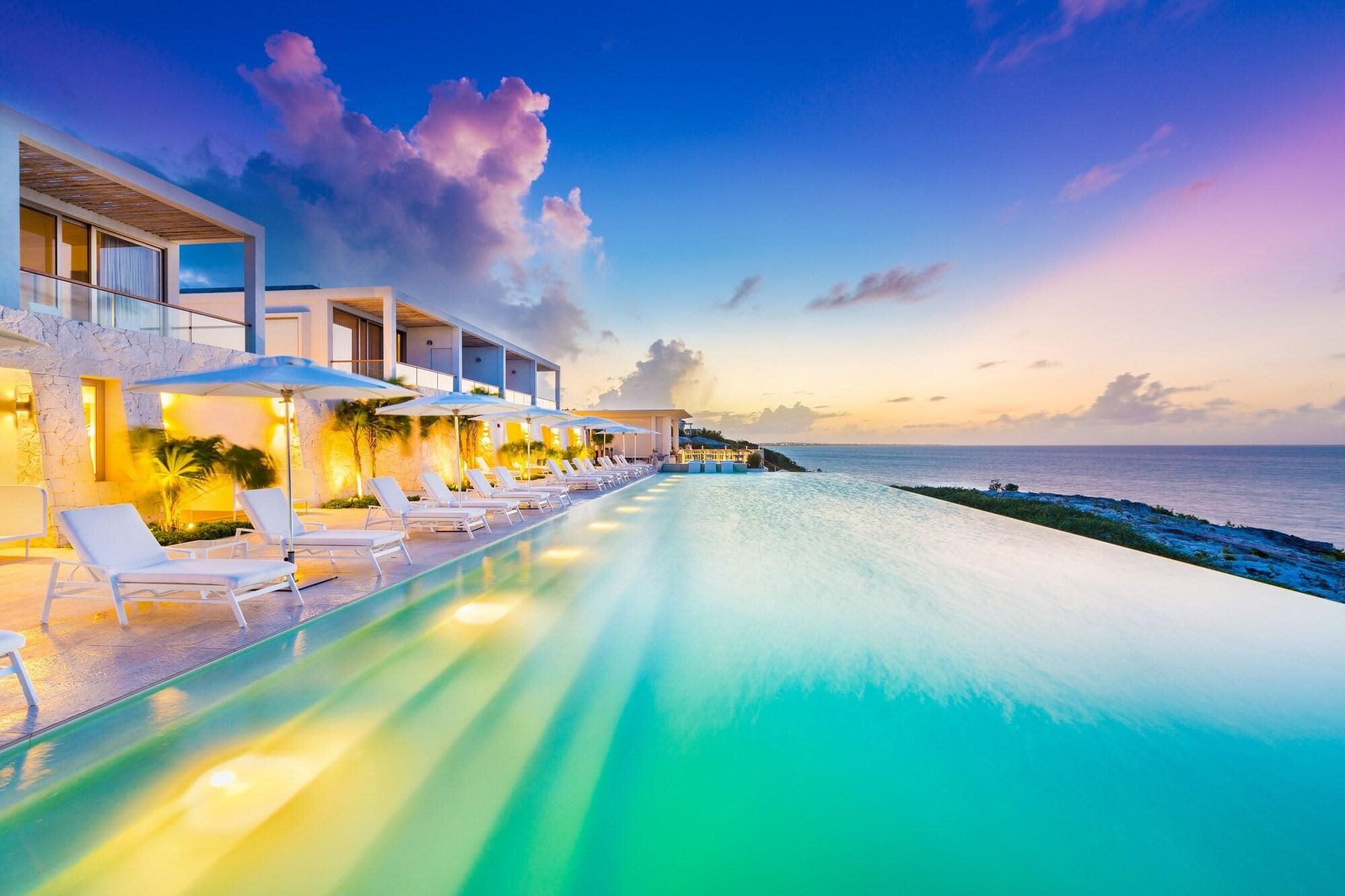 Zona junto a la piscina con sillones y sombrillas, con vista a un cuerpo de agua.