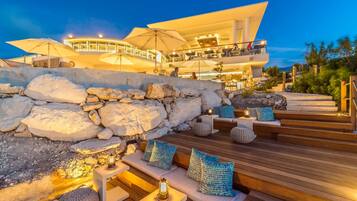 A modern hotel with outdoor seating, a stone wall, and a pool area.