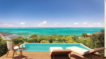 A pool with a view of the ocean, wooden deck, and lounge chairs.