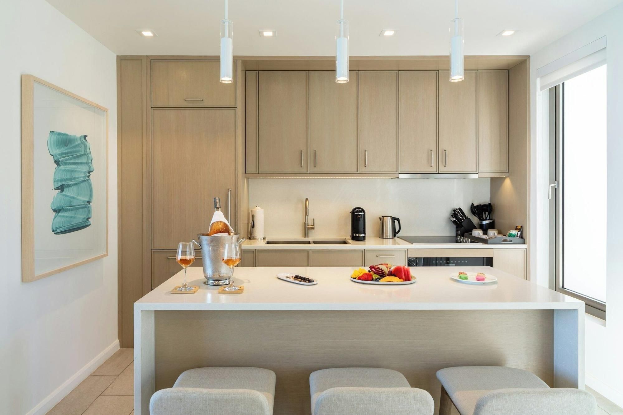 A modern kitchen with a central island, pendant lights, and a large window.