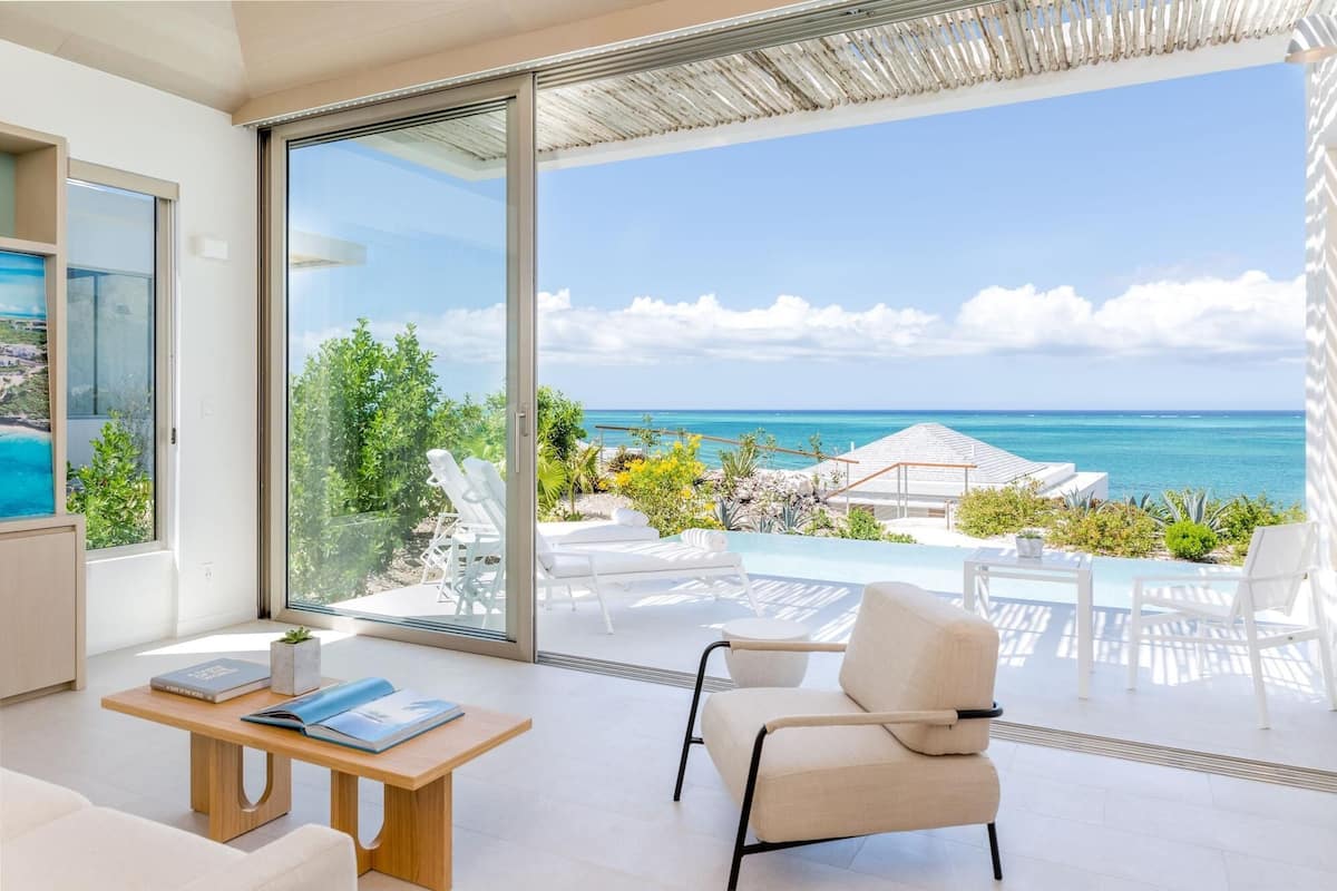 Un salón moderno con un amplio ventanal que da a un balcón con piscina y vistas al océano.