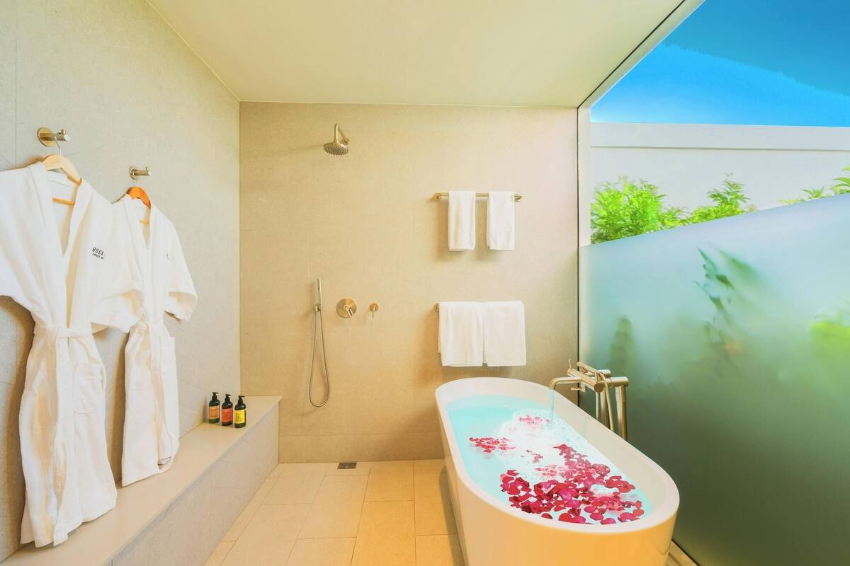 A modern bathroom with a bathtub, shower, and two towels on hooks.