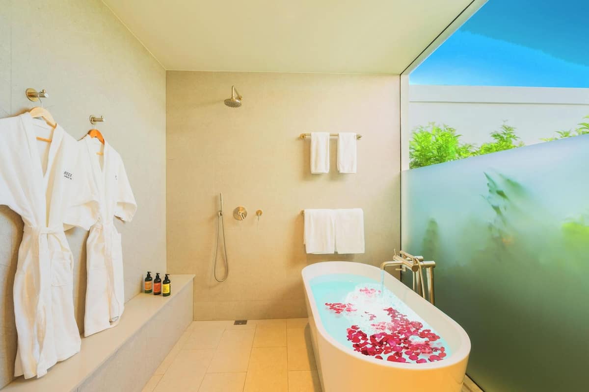 Un baño moderno con bañera, ducha y dos toallas colgadas en ganchos.