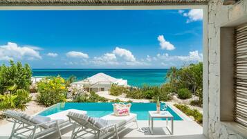 A pool area with lounge chairs, a table with a bottle and glass, and a view of the ocean.