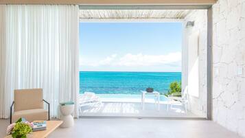 Una habitación con vista al océano, una silla, una mesita con un florero y una silla blanca en el exterior.