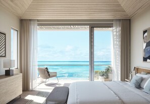 A bedroom with a large bed, a chair, a bedside table, and a view of the ocean. - Rock House (Providenciales)