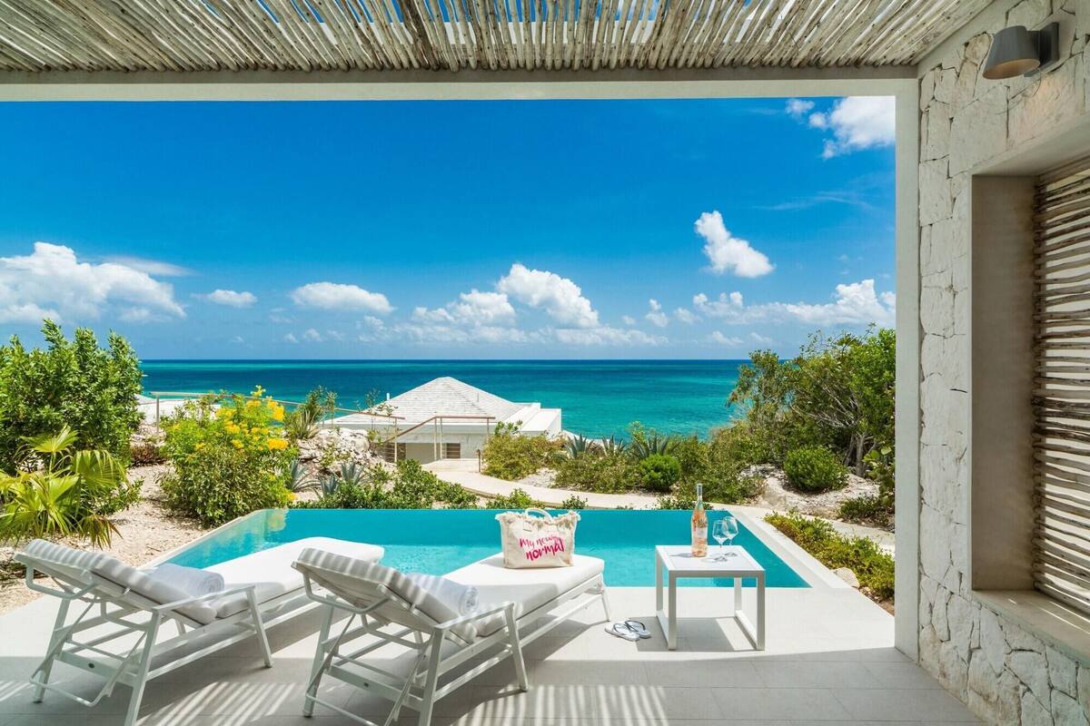 A pool area with lounge chairs, a table, and a view of the ocean.