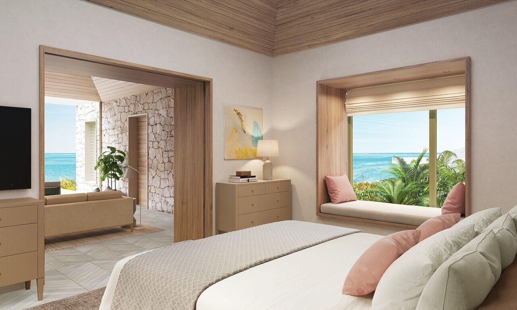 Un dormitorio con cama, cómoda, televisor, ventana y vista al océano, además de una planta.