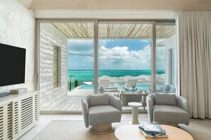 A modern room with a large window overlooking a pool and ocean, two armchairs, a coffee table, and a flat-screen TV. - Rock House (Providenciales)